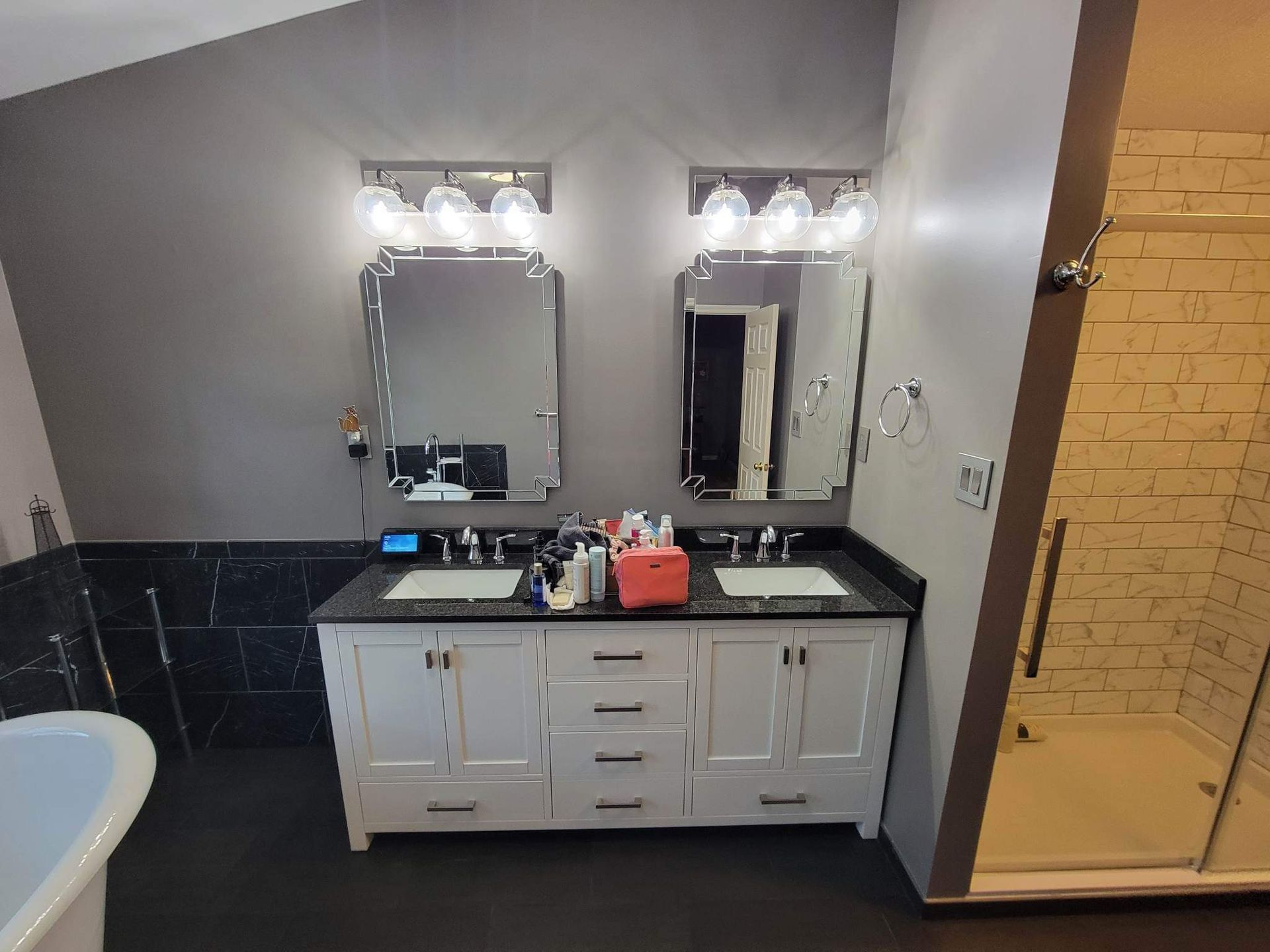 Bathroom with double vanity, two mirrors, and a glass shower. Dark walls and flooring.