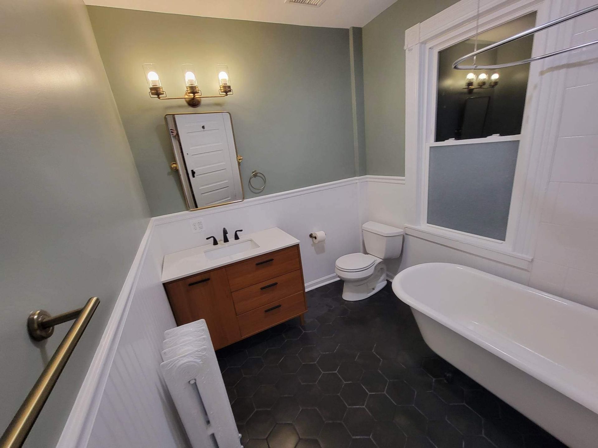 Bathroom with white bathtub, toilet, vanity, and black hexagon tile floor. Light green walls.