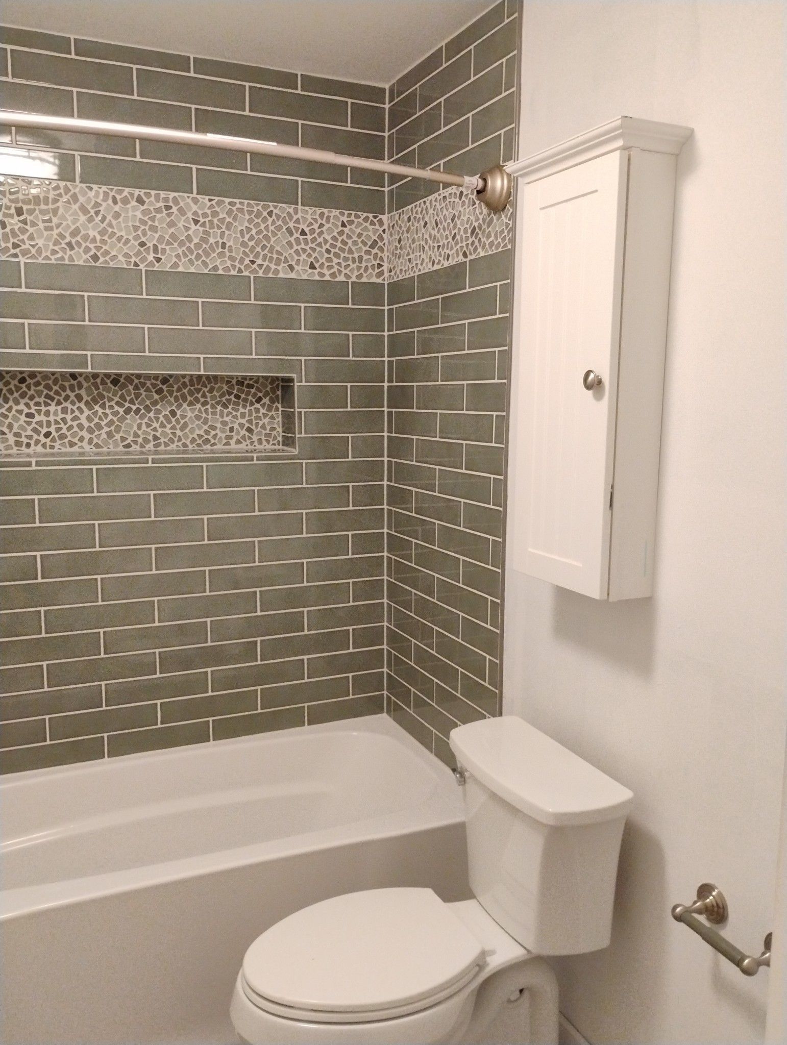 Bathroom with green tiled shower, white tub and toilet, and white cabinet.
