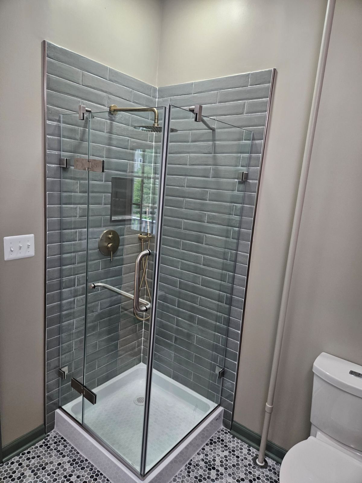 Modern shower with glass doors, gray tiled walls, chrome fixtures, and patterned floor.