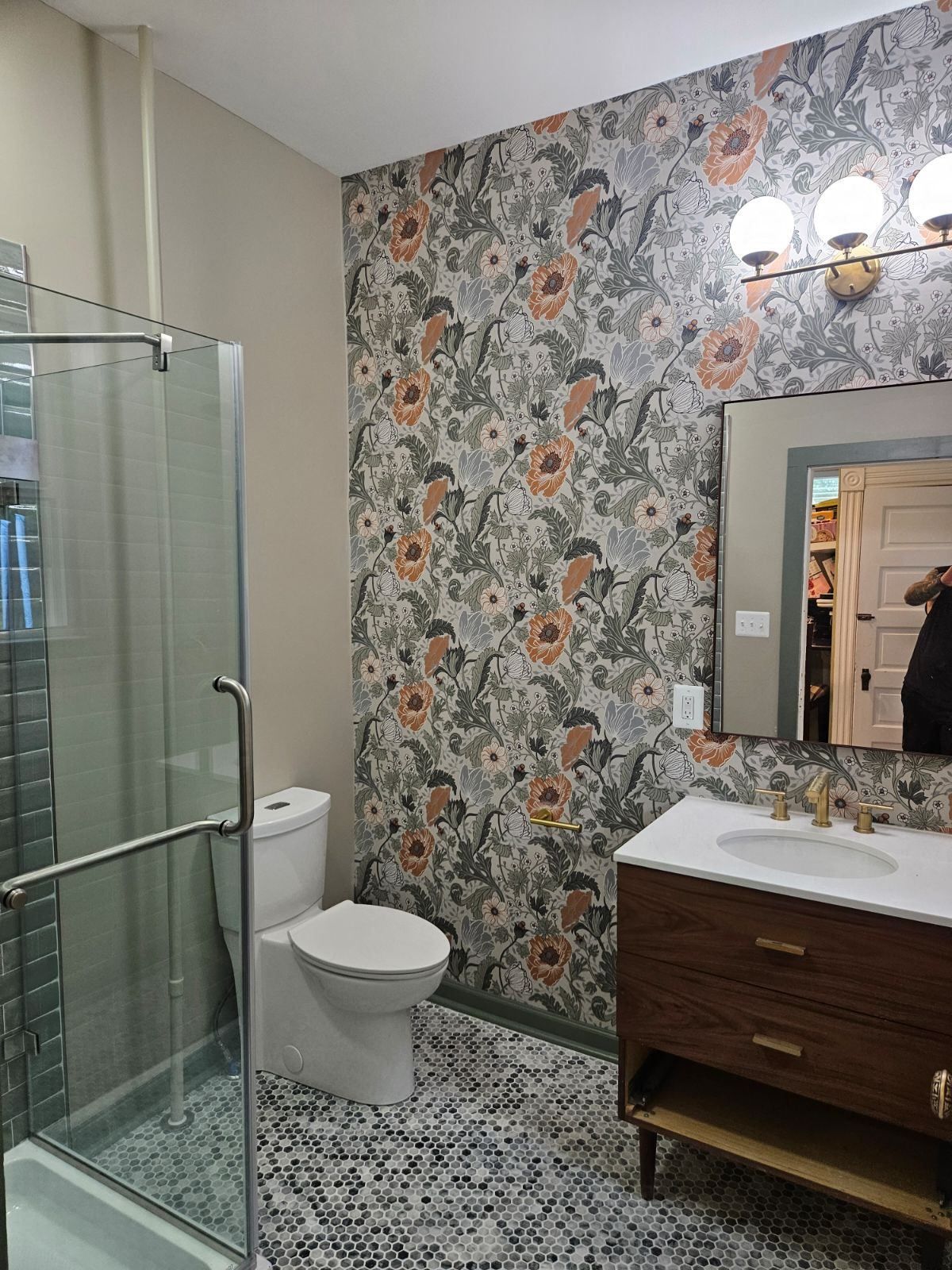 Bathroom with floral wallpaper, glass shower, vanity with sink, and patterned floor tiles.
