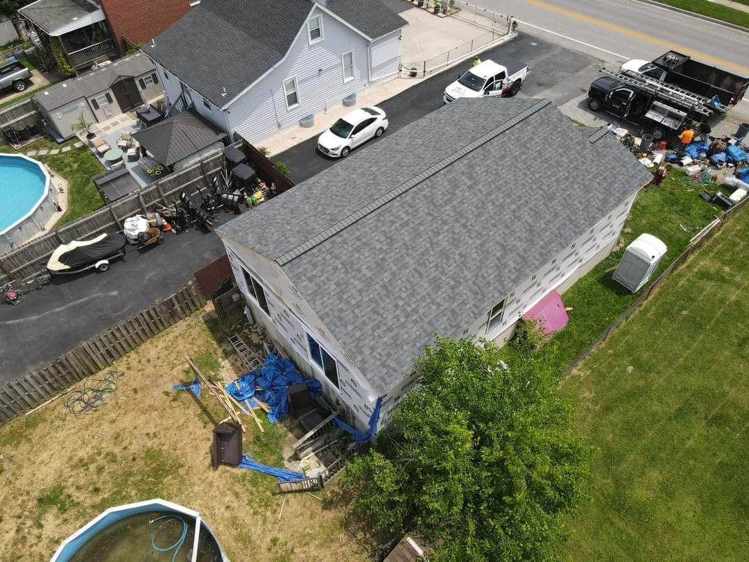 Aerial view of a house with a gray roof and backyard, a pool, and cars parked in front.