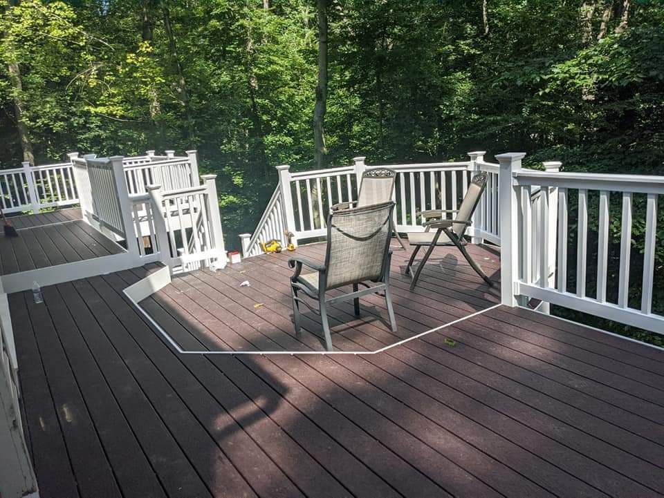 Wooden deck with white railing, chairs, and stairs surrounded by trees.