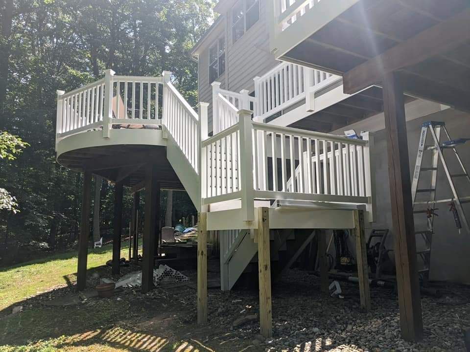 Multi-level deck with white railing. Wooden posts support the structure in a backyard setting.