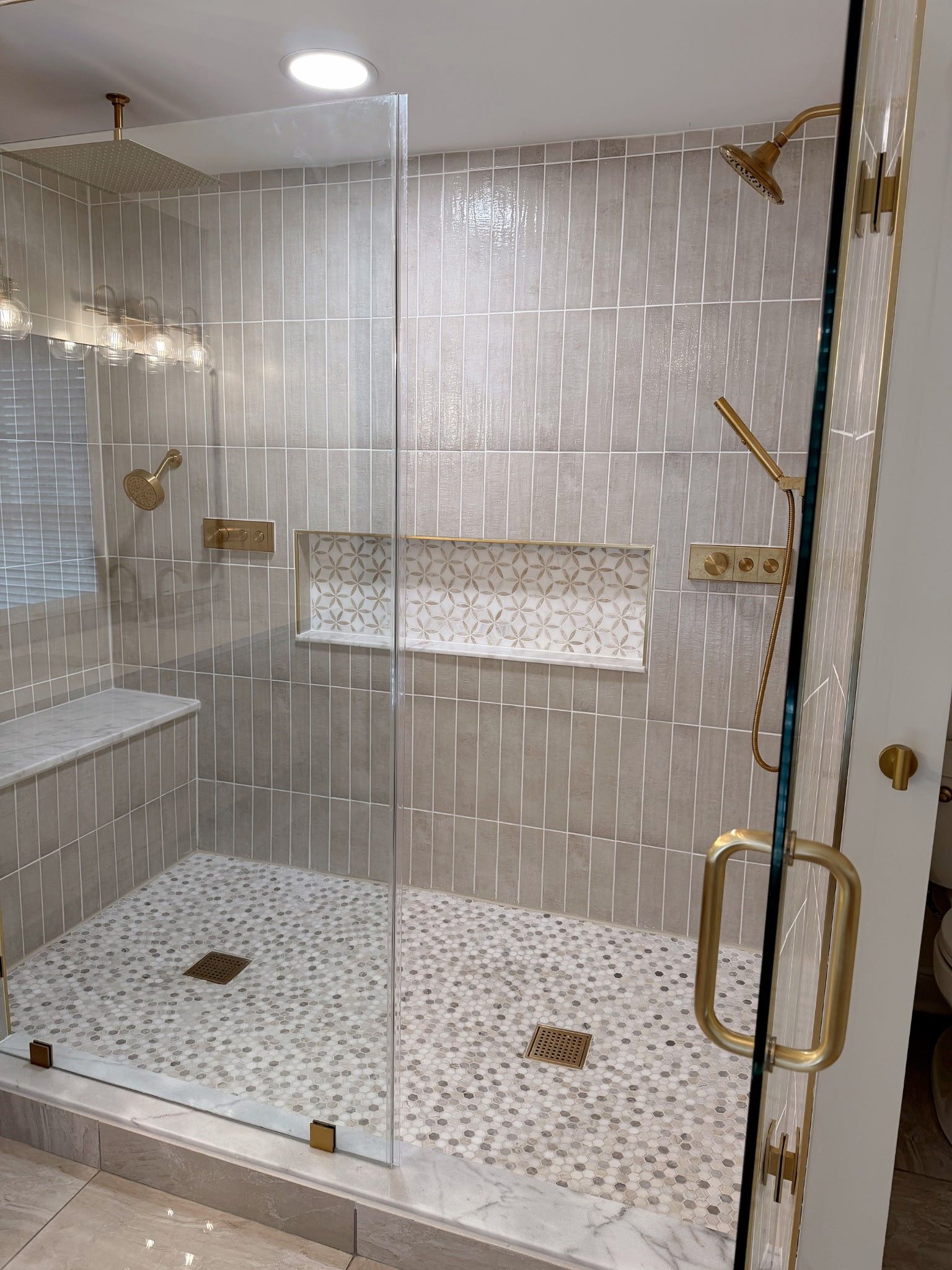 Modern shower with gold fixtures, gray and white tile, glass door.