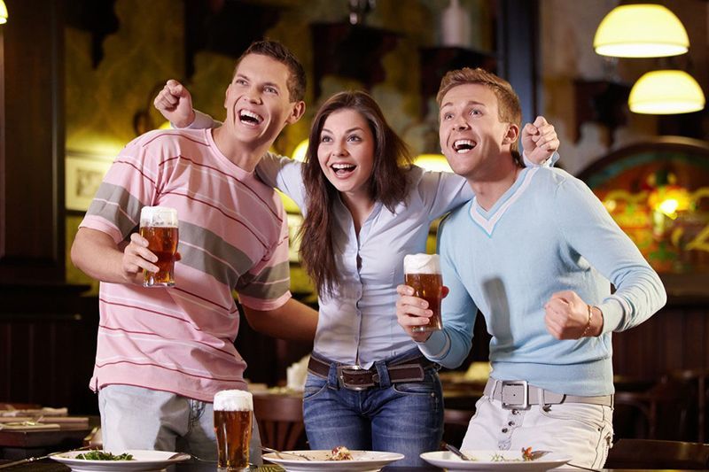 Three people are holding beer glasses in a restaurant.