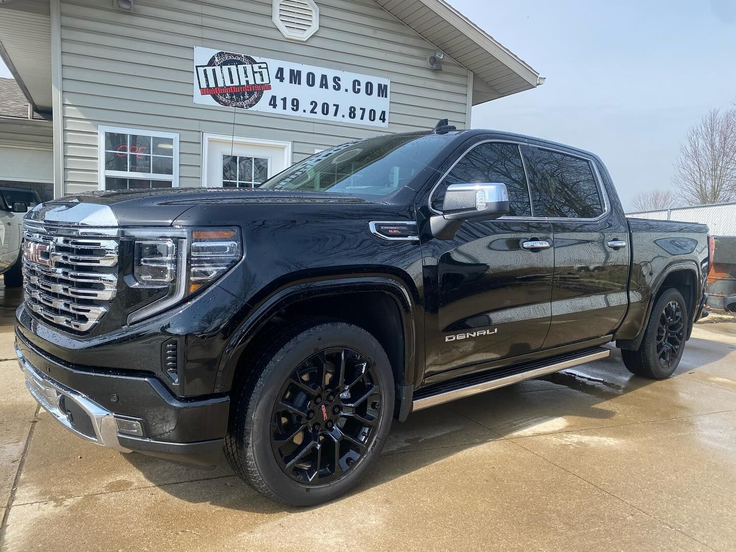 Black GMC Sierra truck parked in front of a building with business signage.