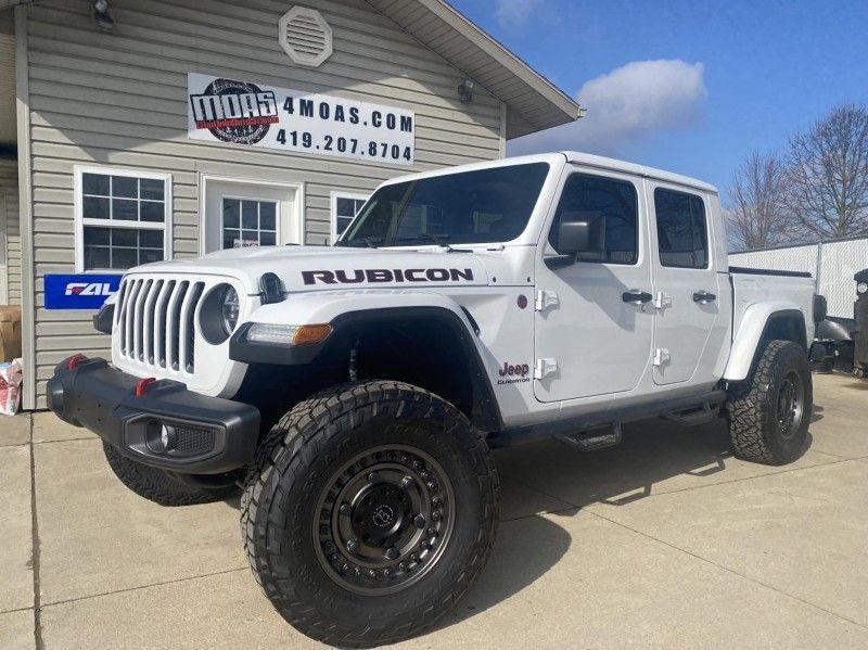 White Jeep Gladiator Rubicon pickup truck parked in front of a building with a business sign.