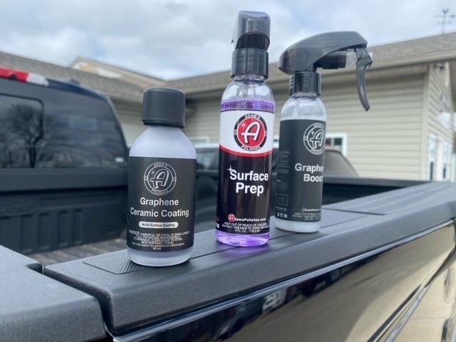 Three car detailing products on a truck bed: ceramic coating, surface prep, and graphene booster.
