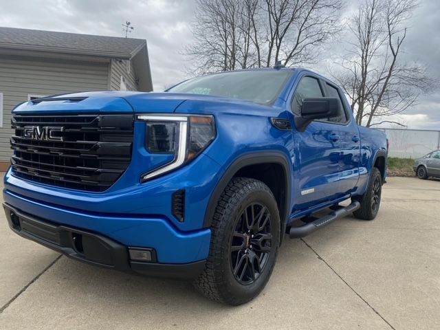 Blue GMC Sierra truck with black grille and wheels parked outside.