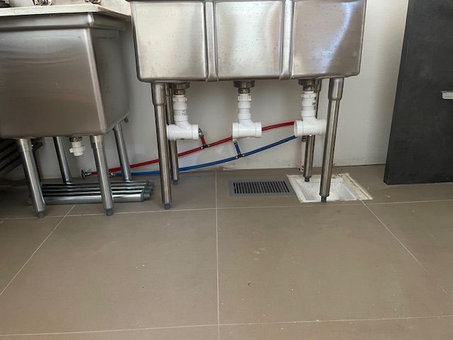 Stainless steel triple sink with white plumbing and gray tiled floor.