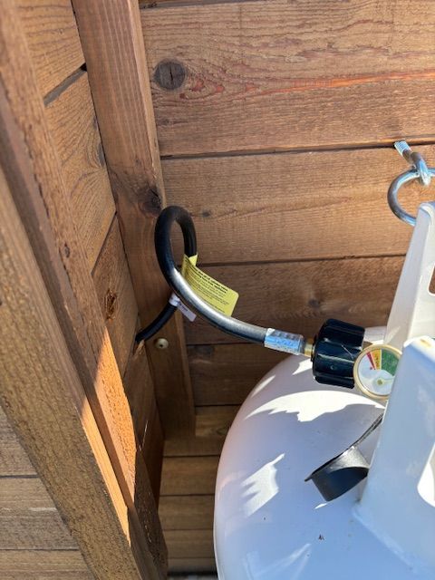 Propane tank with hose connected, secured near wooden structure.