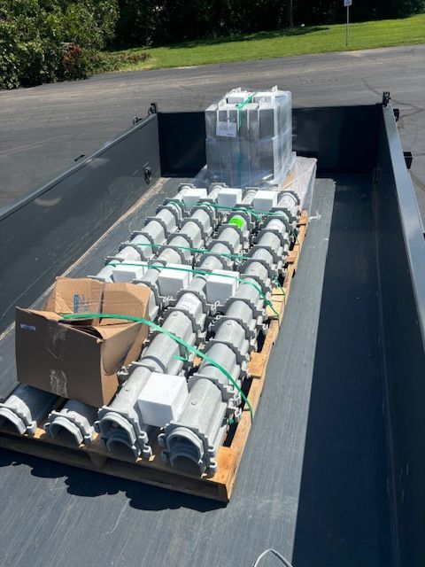 A pallet of equipment loaded in a black truck bed. Gray cylinders with white boxes and a cardboard box.