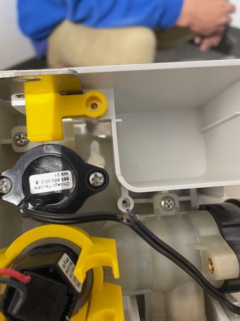 Close-up view of the inside of a white plastic device with yellow and black components, wires, and screws.