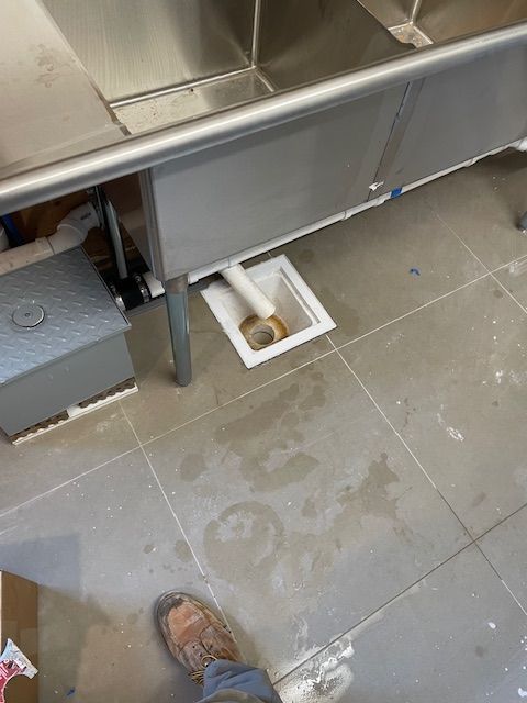 Stainless steel commercial sink, plumbing exposed, on a tiled floor.