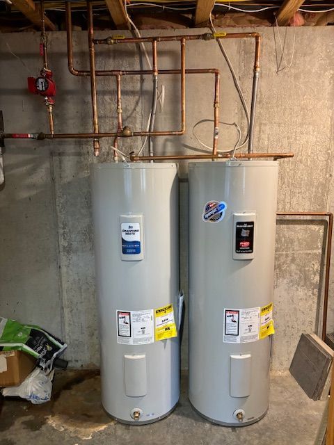 Two cylindrical water heaters, copper piping, basement setting.