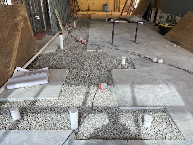Construction site floor, gravel between concrete squares, pipes, electrical cords.