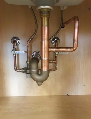 Copper plumbing under a sink: pipes, valves, and a U-shaped drain.
