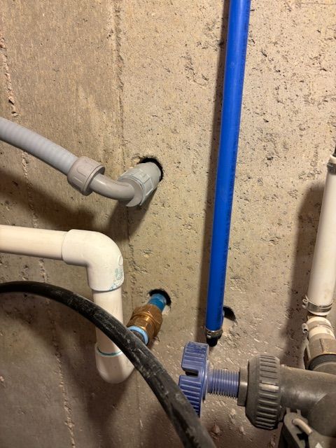 Pipes of various colors emerging from a concrete wall with a blue valve.