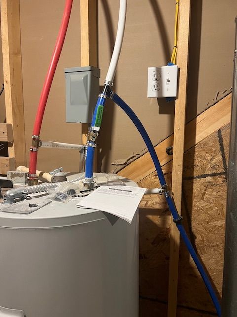 Water heater plumbing: red and blue pipes, white PEX, electrical components in a wall-framed utility room.