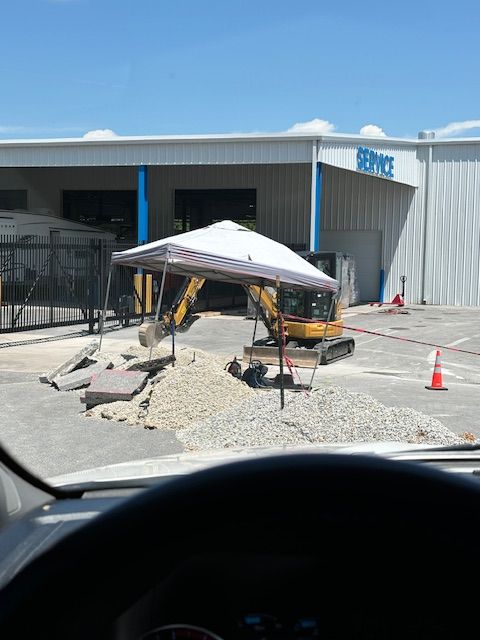 Yellow excavator digging under a white tent in front of a service building.