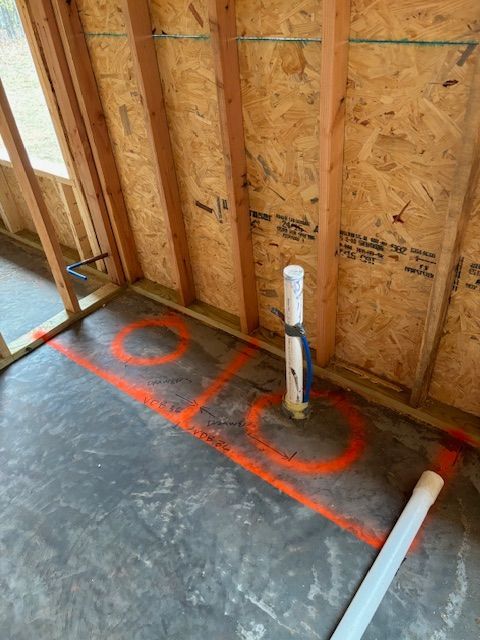 Bathroom construction: Orange markings on concrete floor indicate plumbing layout, vertical pipe in the center.