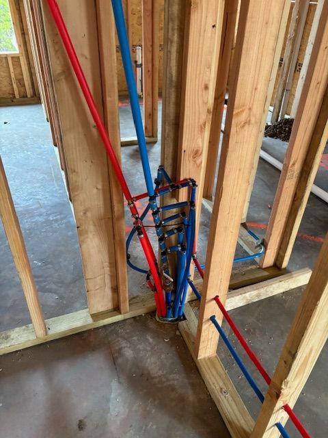 Plumbing pipes in a wooden wall frame: Red and blue PEX tubing, construction site interior.
