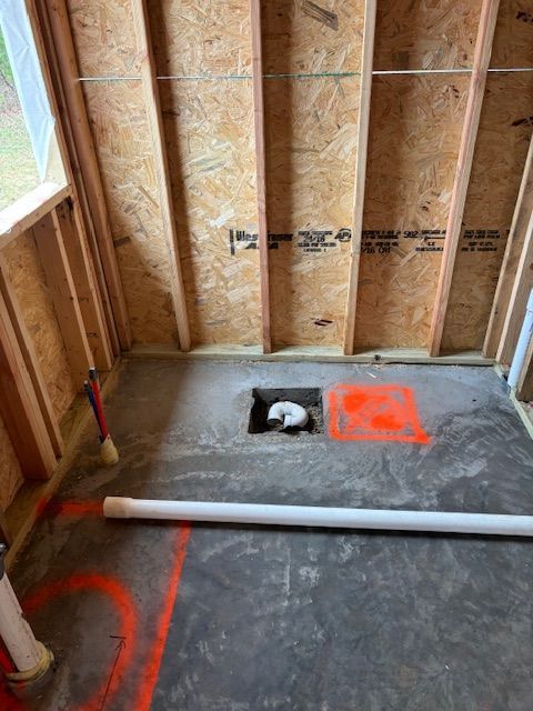 Bathroom construction in progress; concrete floor with drain pipe; wood framing; orange markings.