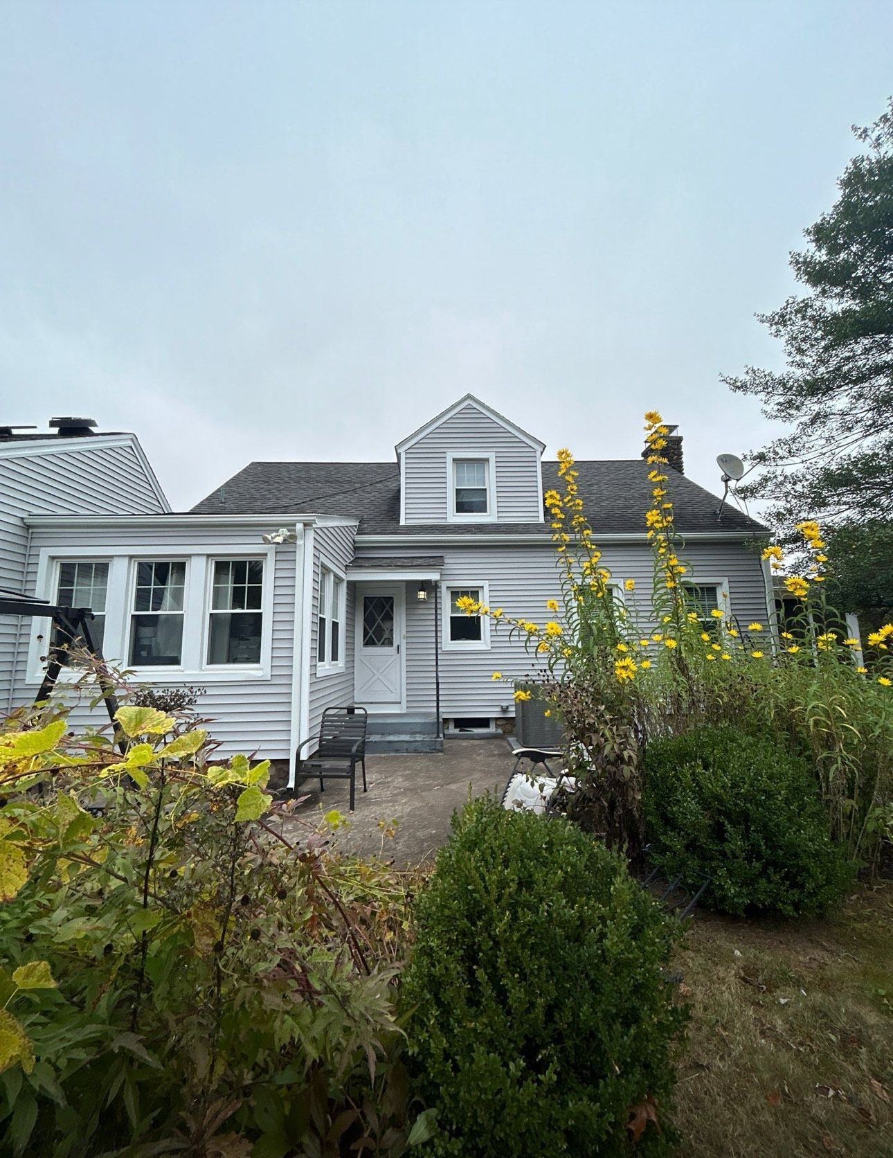 Gray house exterior with plants, small patio, and cloudy sky.