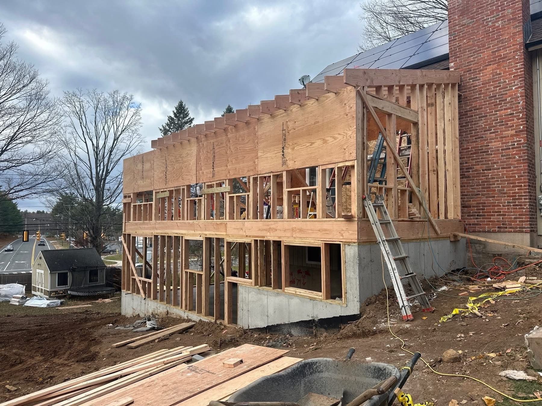 Construction site: new wooden frame addition to brick building. A person is on a ladder. Cloudy sky.