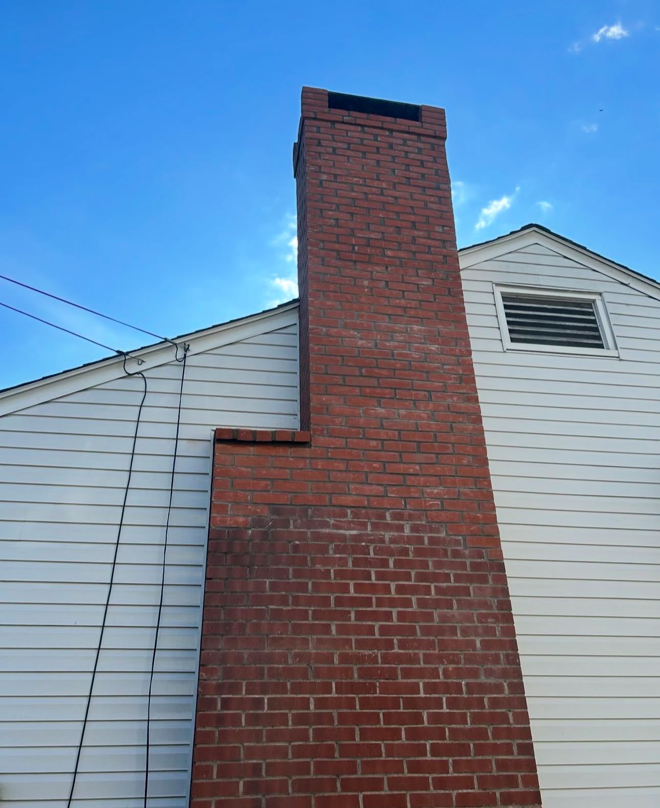 Red brick chimney against a white-sided house and blue sky.