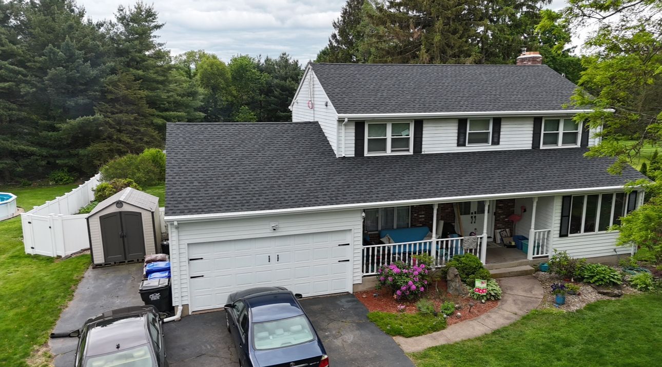 Two-story white house with a black roof, attached garage, and a driveway with two cars.