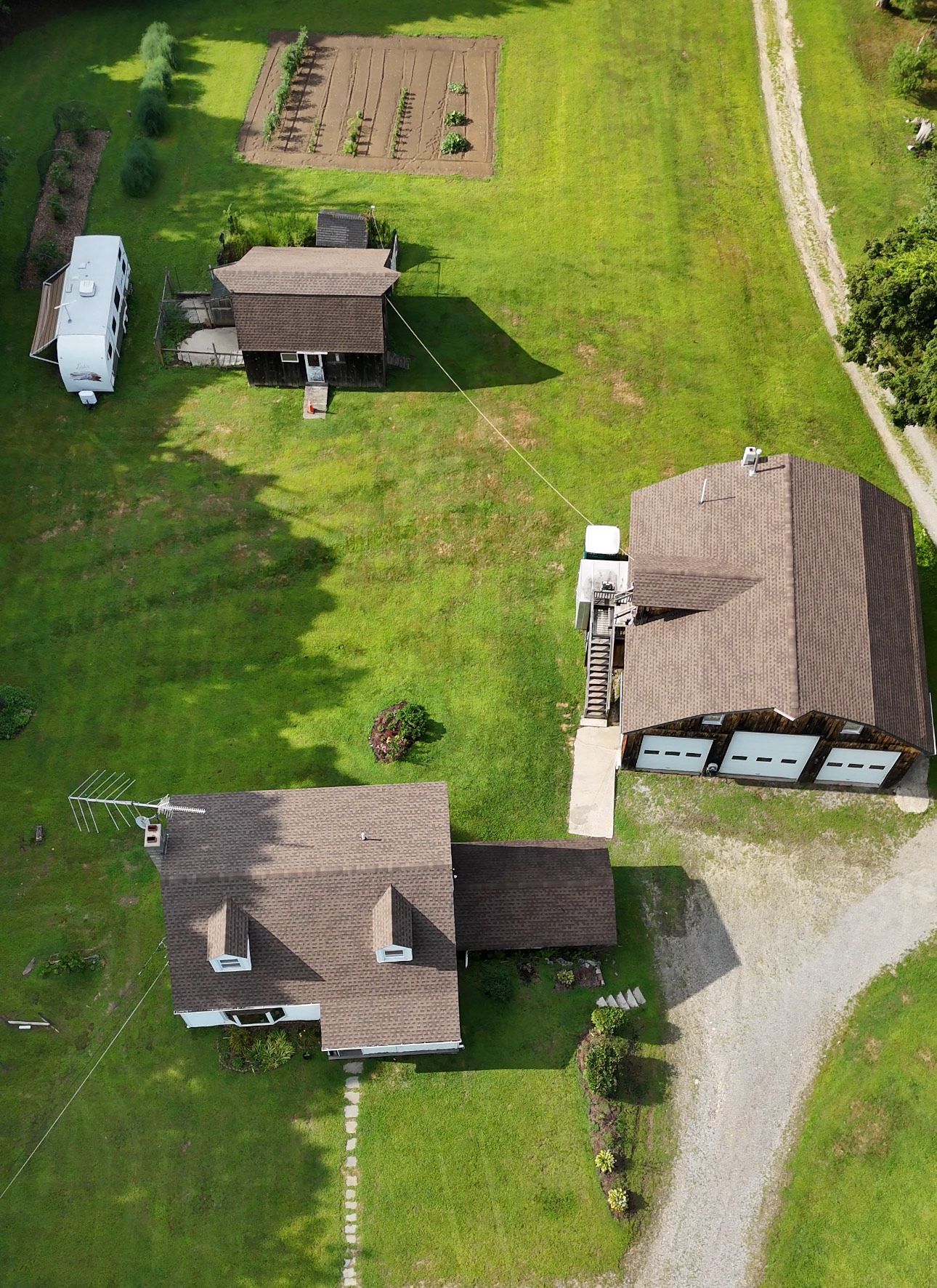 Aerial view of a farm with several buildings, a garden, and a gravel driveway on a grassy landscape.