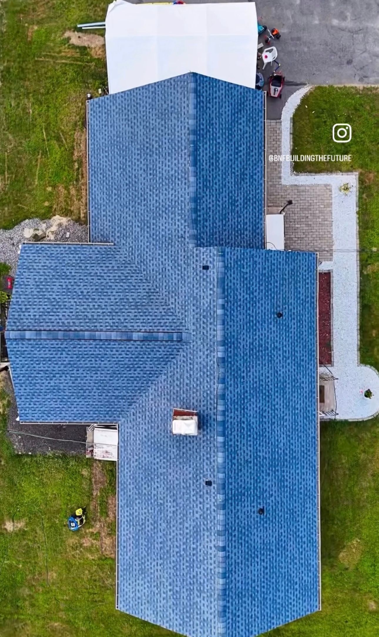 Aerial view of a blue-roofed building on green grass, with a white structure attached.