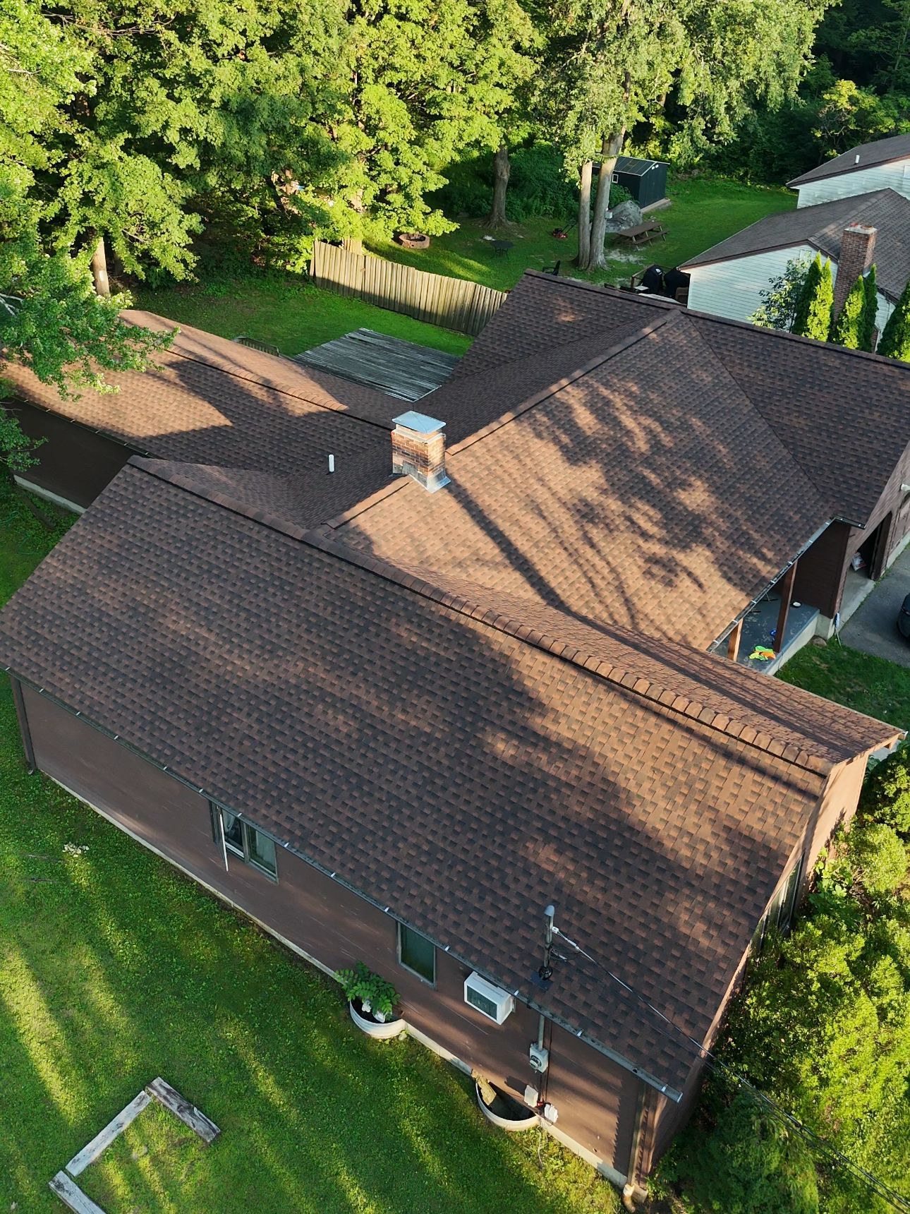 Brown roofed house surrounded by green grass and trees on a sunny day.