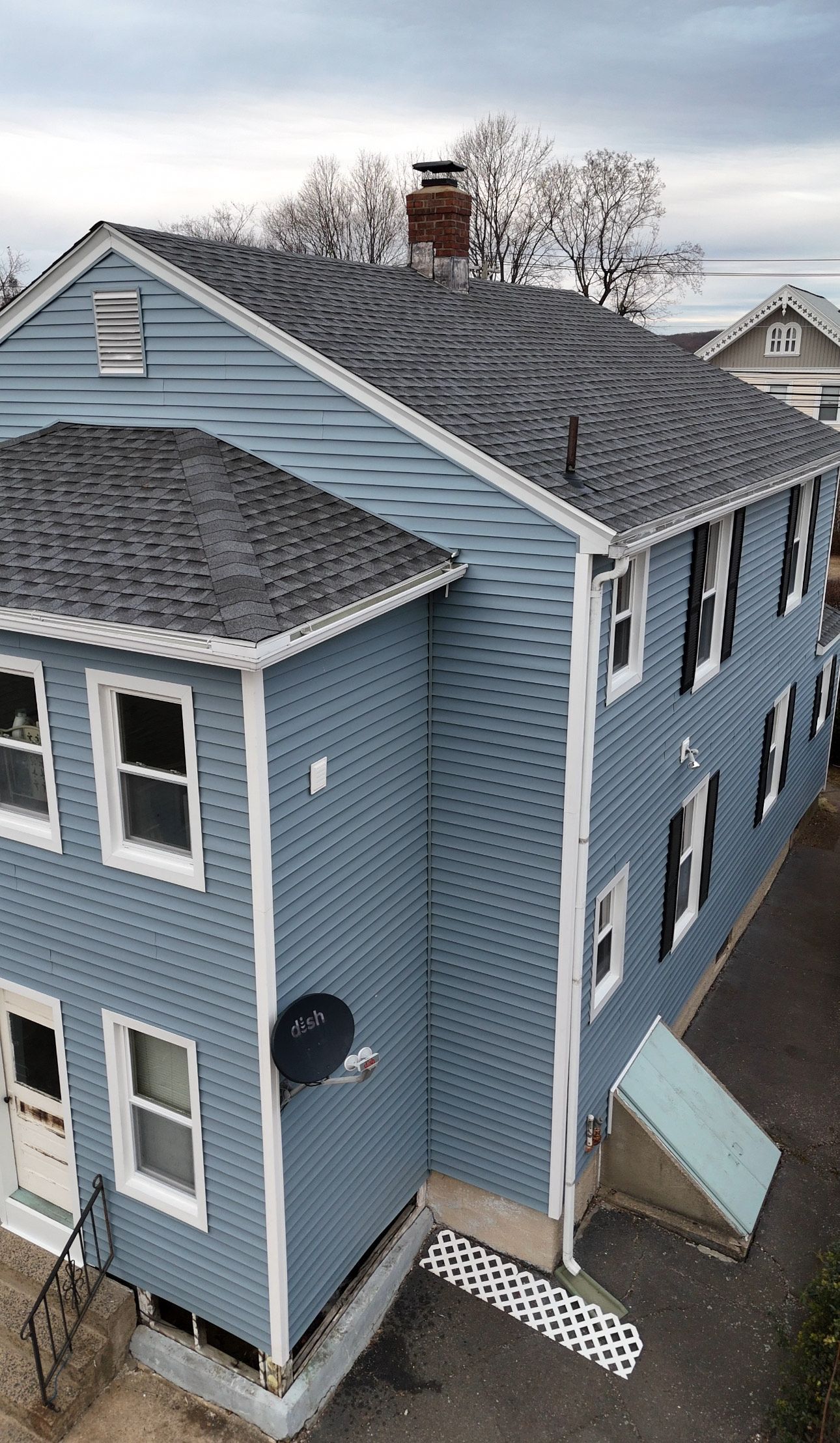 Two-story blue house with gray roof, windows, and white trim. Satellite dish on the side.