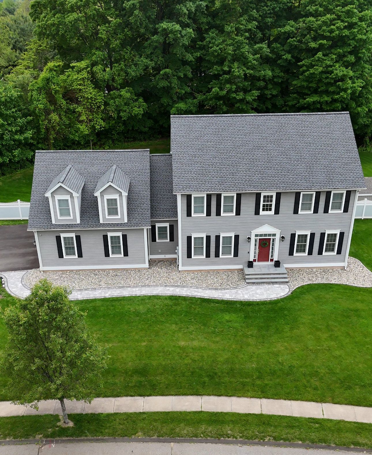 Gray-sided two-story house with black shutters, dormers, and gray roof, in front of a green yard and trees.