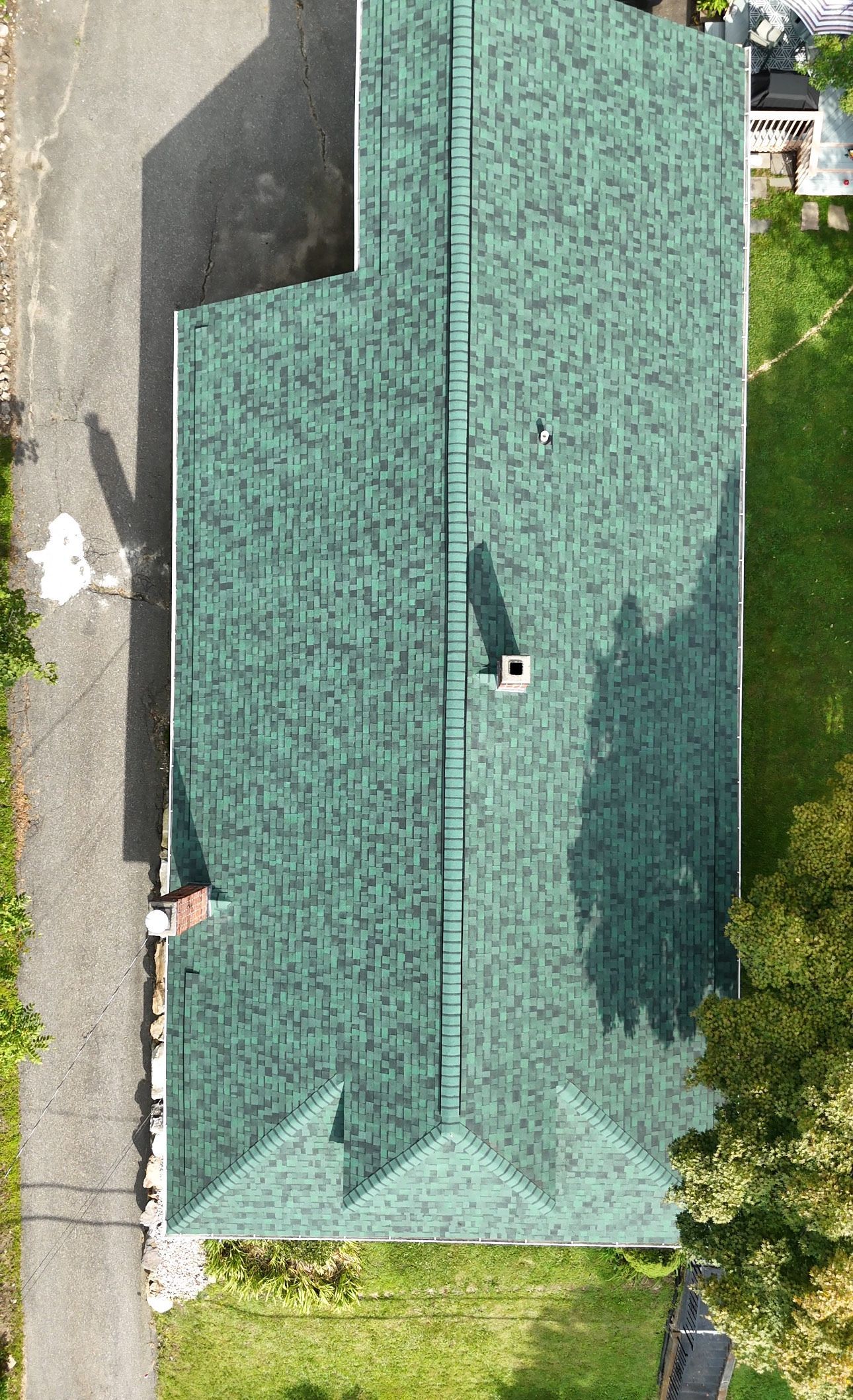 Green shingled roof of a house with a chimney and a small addition.