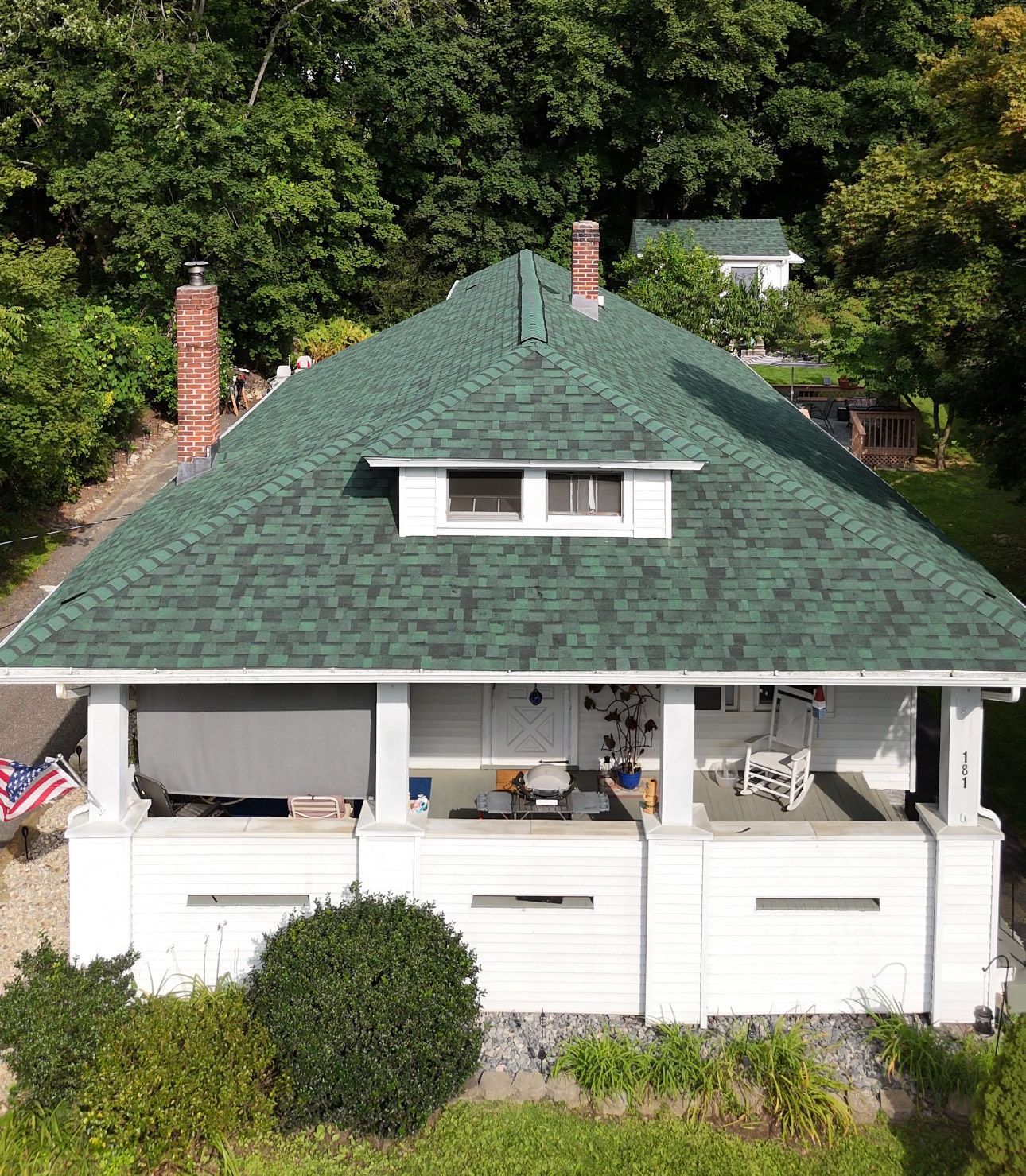White Craftsman home with a green roof surrounded by trees.