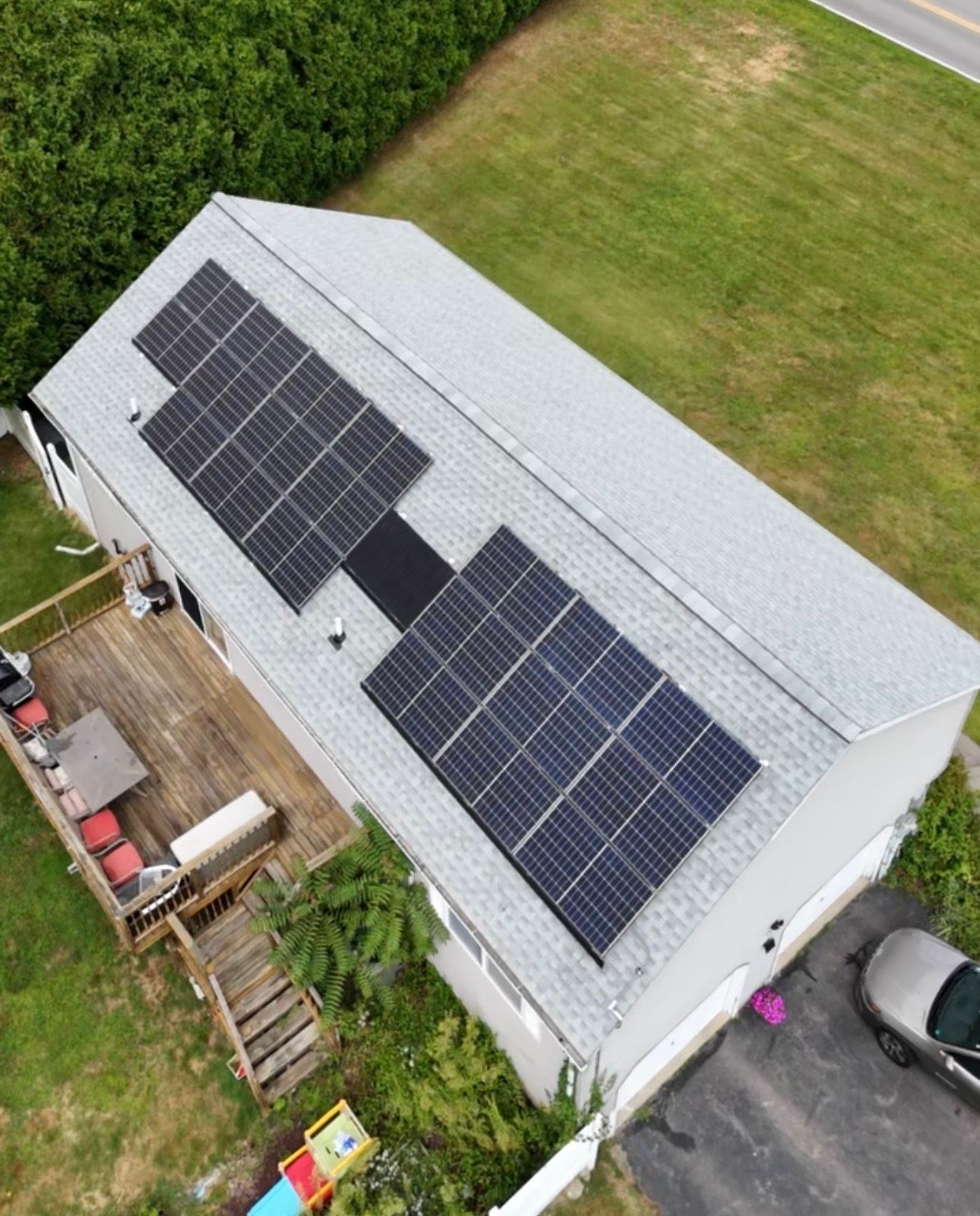 Solar panels on a gray roof of a house with a deck and a car parked in the driveway.