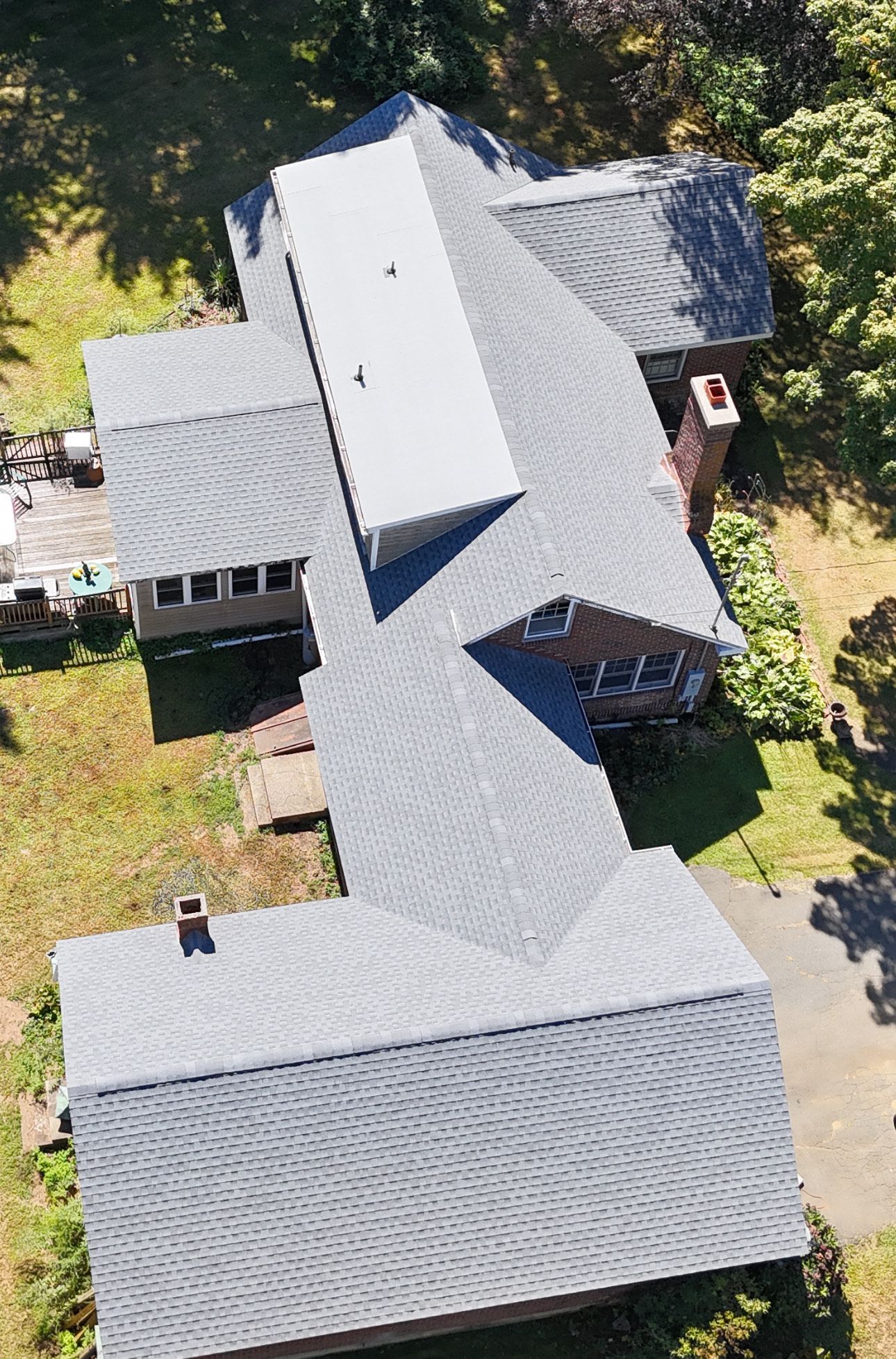 Aerial view of a gray-roofed house with a brick chimney and surrounding greenery.