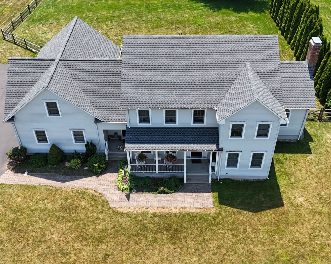 Aerial view of a gray two-story house with a porch, surrounded by green grass and a fence.