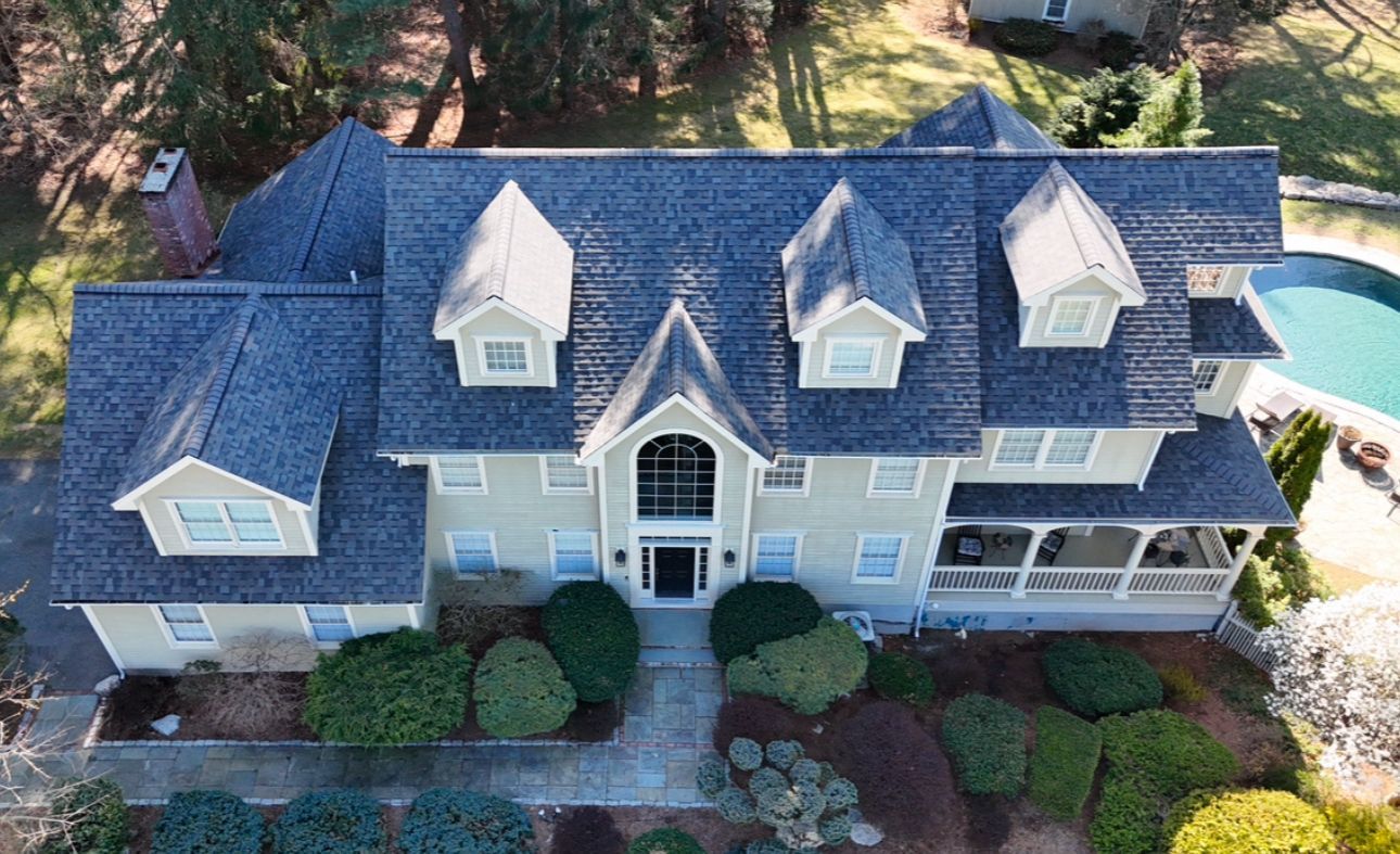 Aerial view of a large, two-story house with a blue roof, white trim, and a swimming pool.