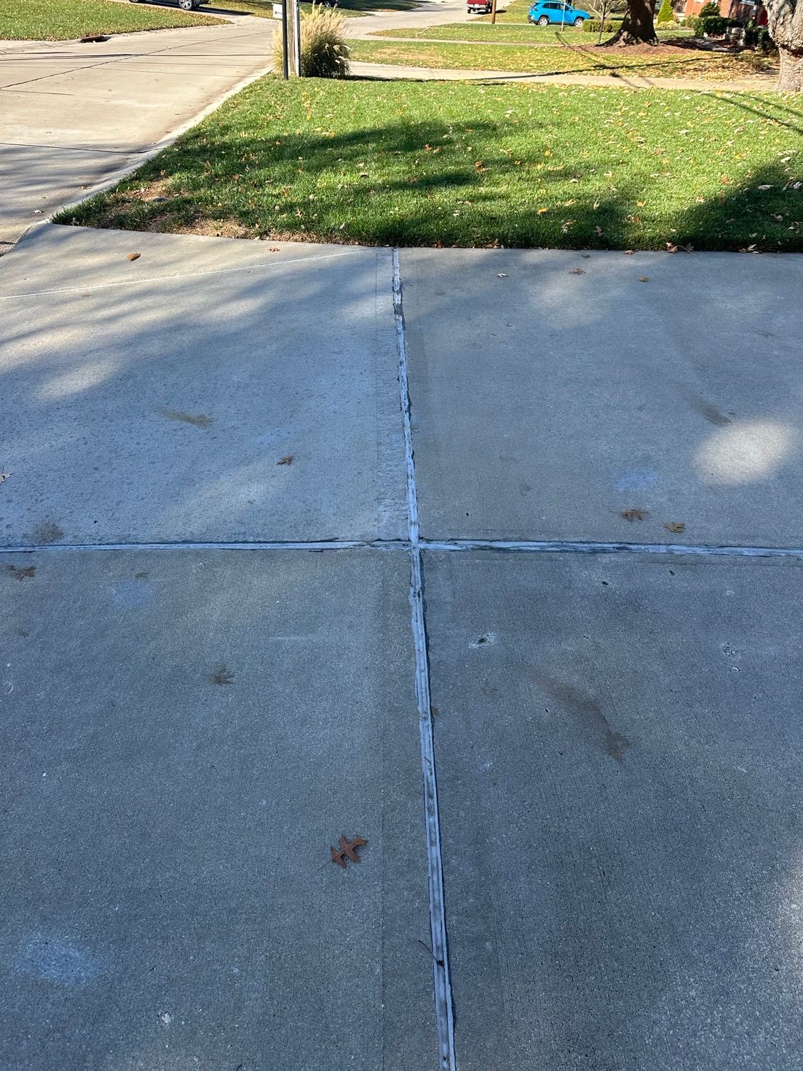 Driveway with concrete slabs and filled expansion joints, with a lawn in the background.