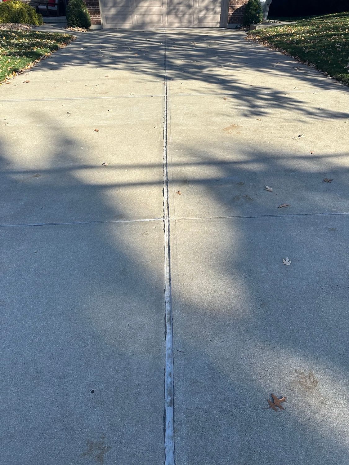 Concrete driveway with vertical and horizontal expansion joints. Sunlight casts shadows.