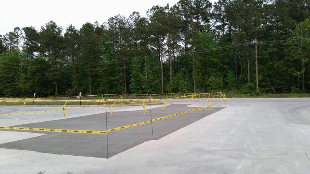 A concrete parking lot with yellow tape around it and trees in the background.