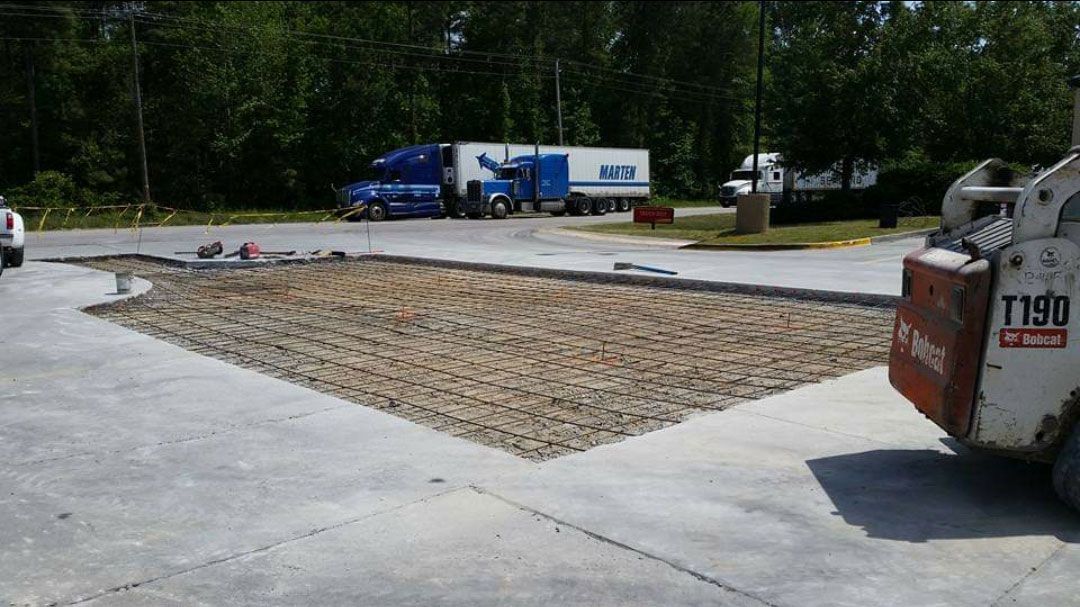 A bobcat is sitting in a parking lot next to a truck.