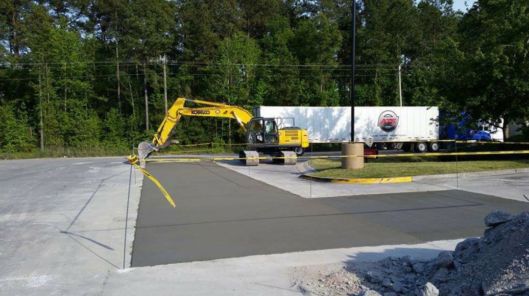A yellow excavator is working on a parking lot next to a truck.