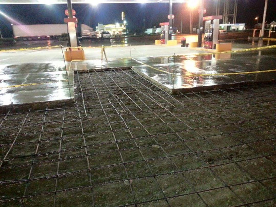 A gas station is being built at night and the concrete is being poured.