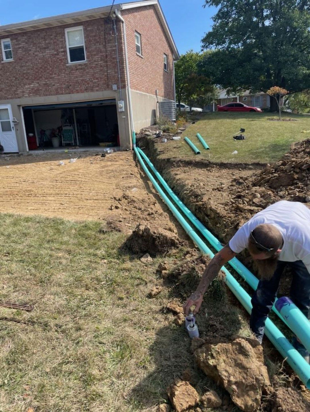 A man is kneeling in the dirt next to a green pipe.